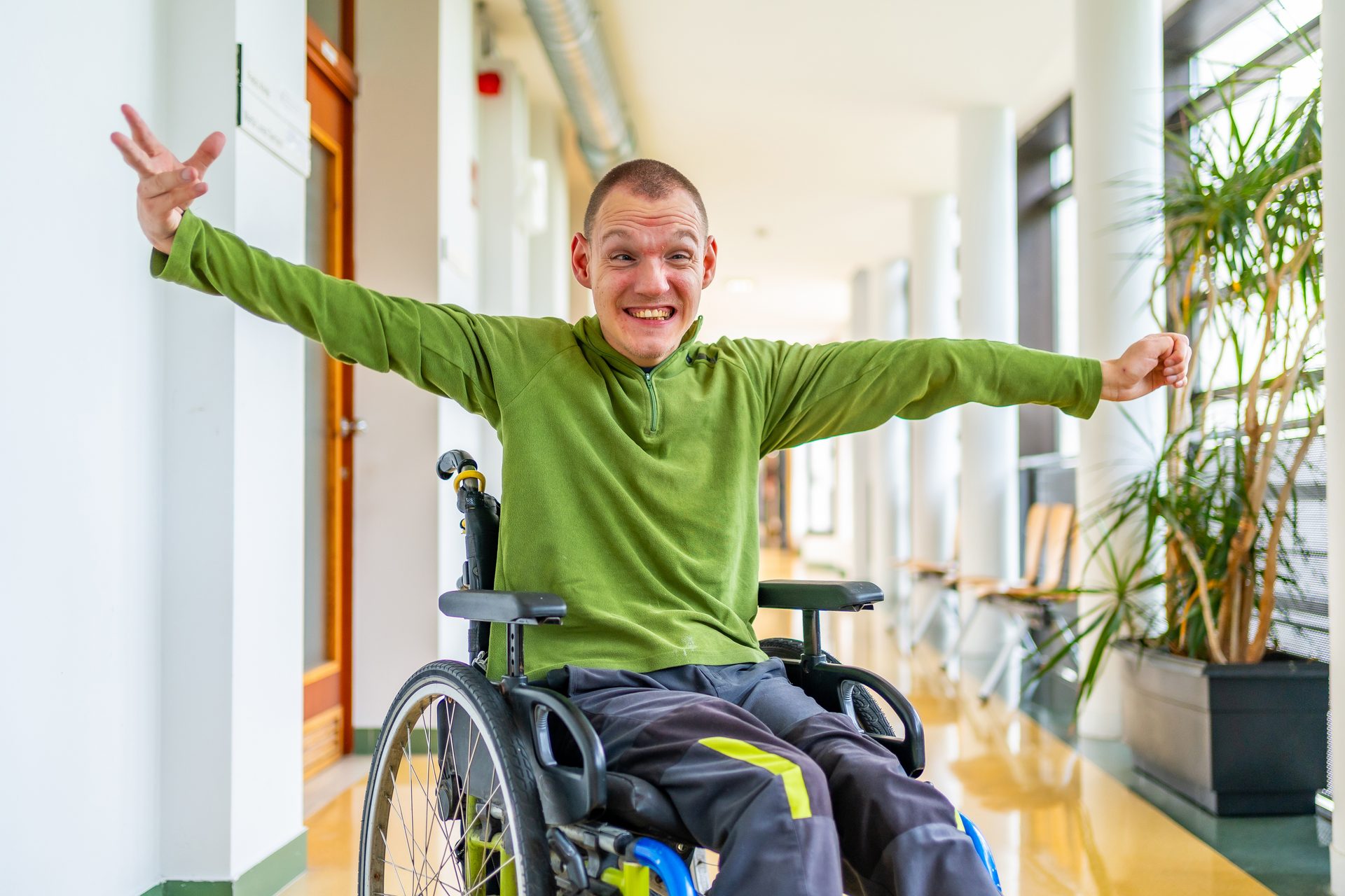 Mann im Rollstuhl in einer Einrichtung in Niedersachsen, lächelnd und mit ausgestreckten Armen
